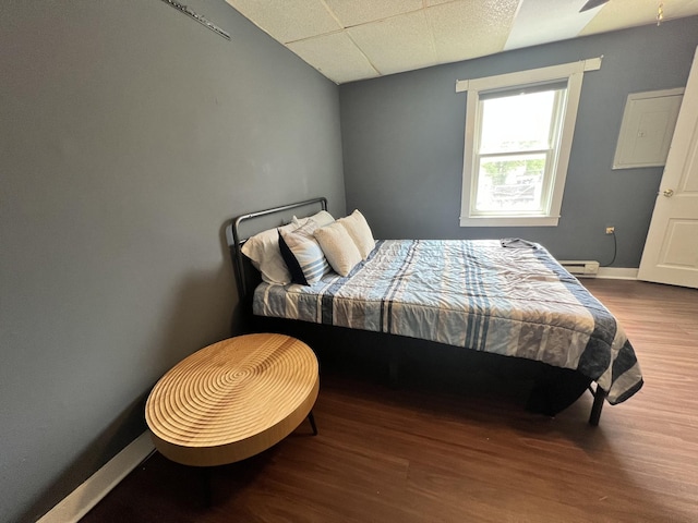 bedroom featuring a paneled ceiling, baseboards, baseboard heating, and wood finished floors