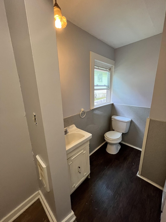 half bathroom featuring toilet, vanity, baseboards, and wood finished floors