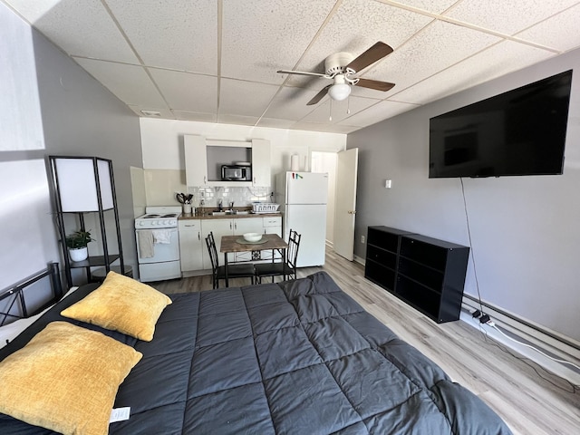 bedroom with a drop ceiling, a sink, freestanding refrigerator, and wood finished floors