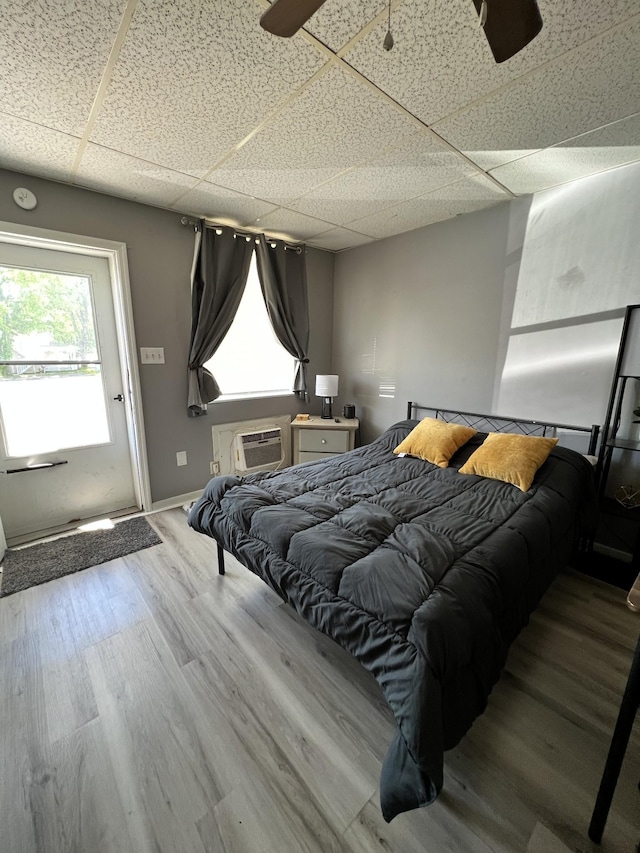 bedroom featuring a drop ceiling, baseboards, an AC wall unit, and wood finished floors