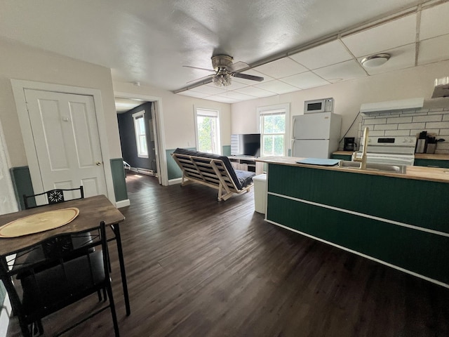 kitchen with white appliances, a ceiling fan, dark wood-style floors, baseboards, and a sink