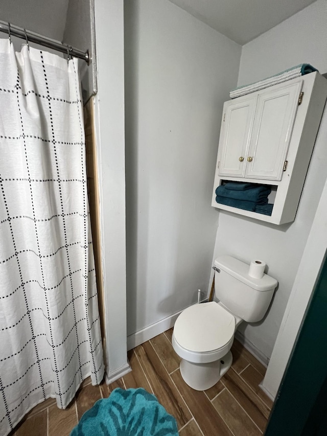 bathroom featuring curtained shower, toilet, baseboards, and wood finish floors