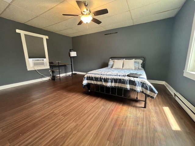 bedroom featuring wood finished floors, visible vents, baseboards, a baseboard radiator, and a drop ceiling