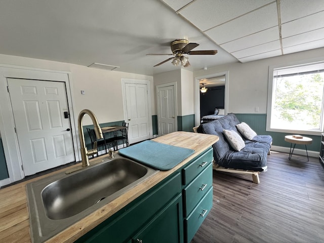 kitchen with a sink, green cabinets, a wainscoted wall, wood counters, and dark wood-style flooring