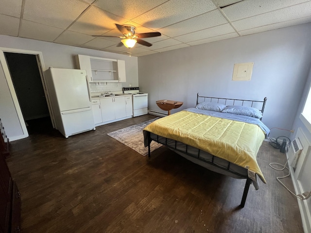 bedroom with a sink, a baseboard heating unit, a drop ceiling, dark wood-style floors, and freestanding refrigerator