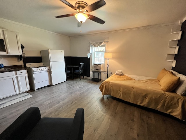 bedroom with a ceiling fan, wood finished floors, freestanding refrigerator, a sink, and crown molding