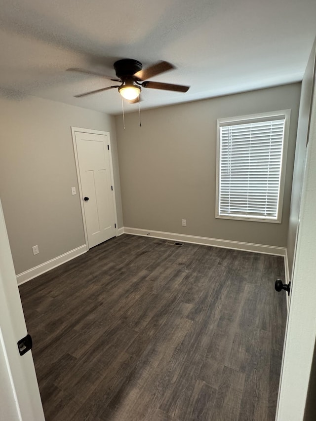 spare room featuring dark wood-type flooring, a ceiling fan, and baseboards