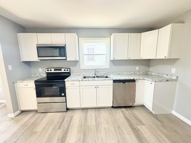 kitchen with light wood finished floors, white cabinets, appliances with stainless steel finishes, and a sink