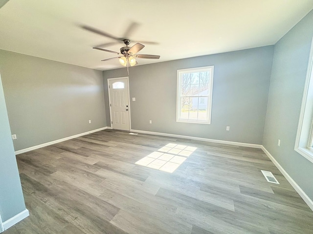 empty room with visible vents, ceiling fan, baseboards, and wood finished floors