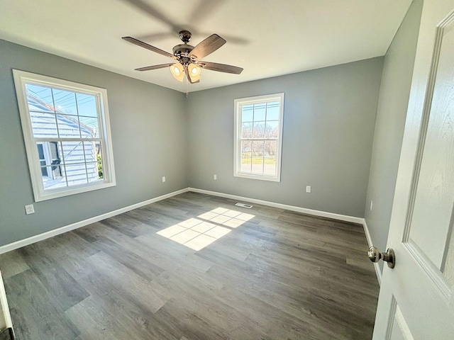 empty room with a wealth of natural light, visible vents, dark wood-type flooring, and baseboards