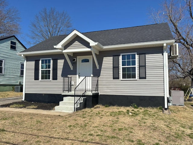 bungalow with a front lawn, central air condition unit, and roof with shingles