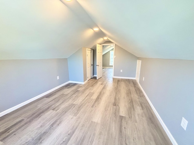 additional living space with lofted ceiling, light wood-type flooring, and baseboards