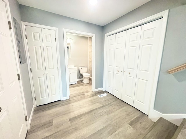 unfurnished bedroom with connected bathroom, baseboards, and light wood finished floors