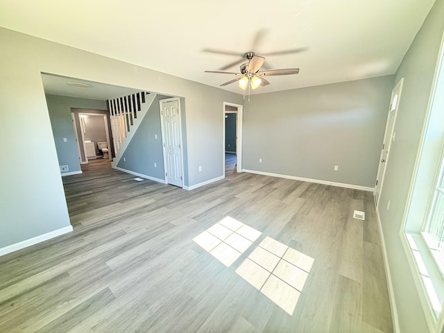 spare room featuring stairs, light wood-style floors, and baseboards