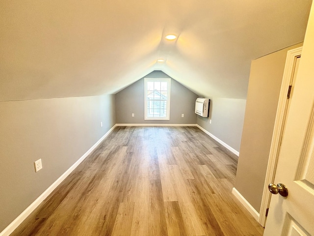 additional living space with vaulted ceiling, heating unit, wood finished floors, and baseboards