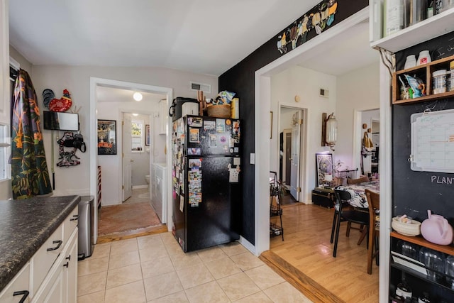 kitchen featuring visible vents, lofted ceiling, light tile patterned flooring, freestanding refrigerator, and dark countertops