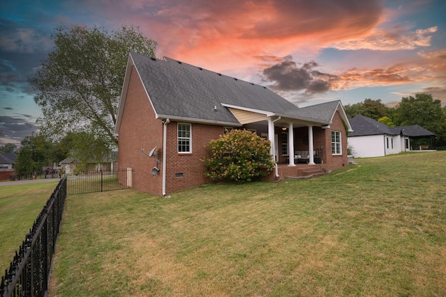 back of property at dusk featuring roof with shingles, a yard, a fenced backyard, crawl space, and brick siding