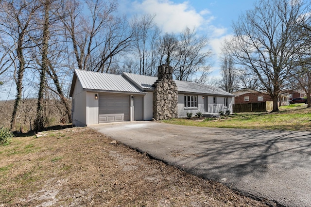 single story home with a front lawn, a chimney, metal roof, a garage, and driveway