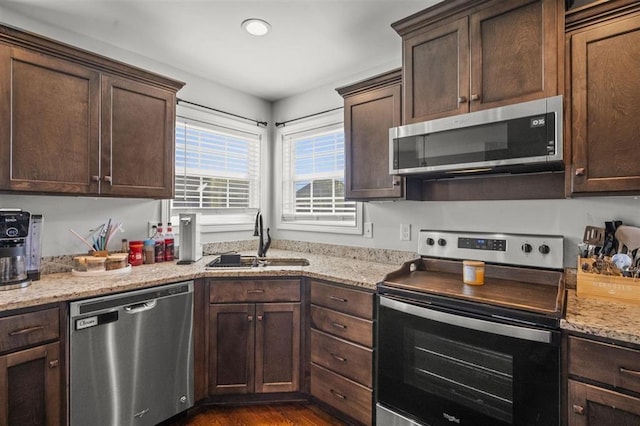 kitchen with a sink, dark brown cabinetry, light stone countertops, and stainless steel appliances