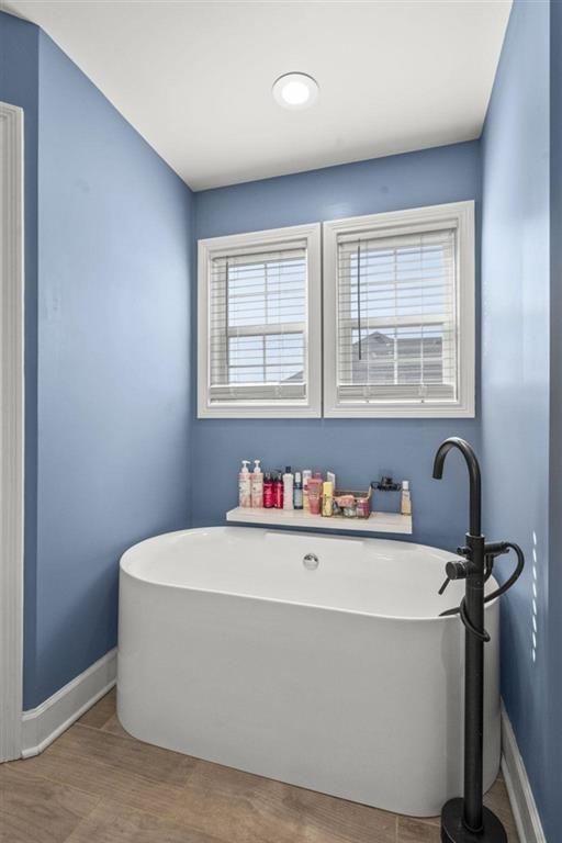 full bathroom with a wealth of natural light, baseboards, a soaking tub, and wood finished floors