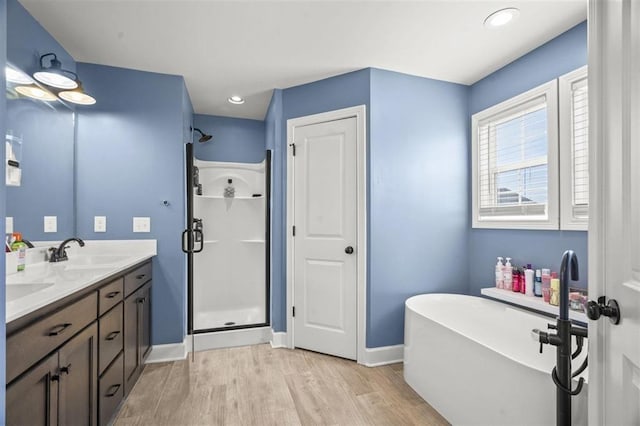 bathroom featuring a freestanding bath, a stall shower, wood finished floors, and a sink