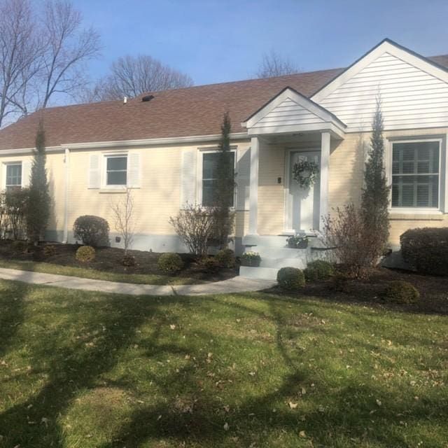 view of front of property featuring brick siding, a front yard, and a shingled roof