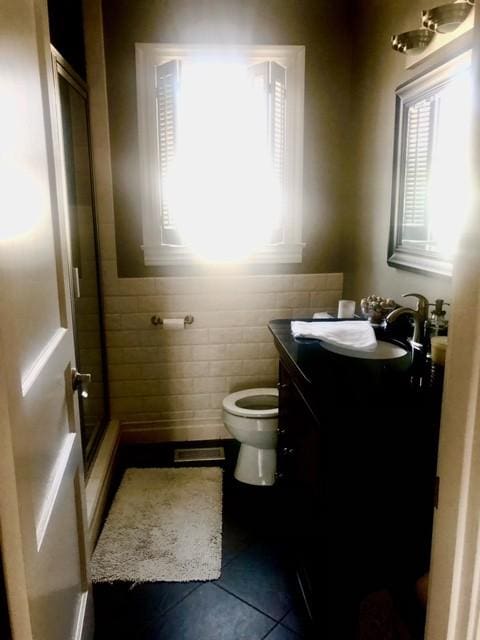 bathroom featuring tile patterned floors, toilet, a stall shower, tile walls, and vanity