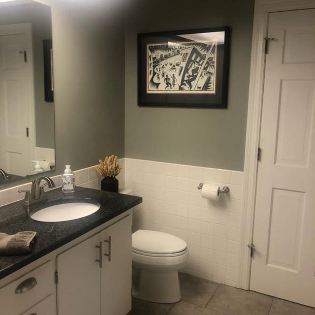 half bathroom featuring vanity, a wainscoted wall, tile patterned floors, toilet, and tile walls