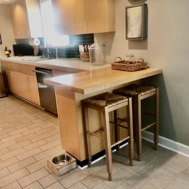 kitchen featuring stainless steel dishwasher, a peninsula, a breakfast bar area, light countertops, and decorative backsplash