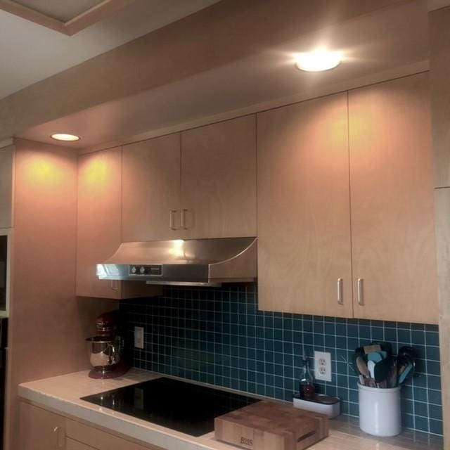 kitchen with under cabinet range hood, decorative backsplash, light countertops, and black electric cooktop