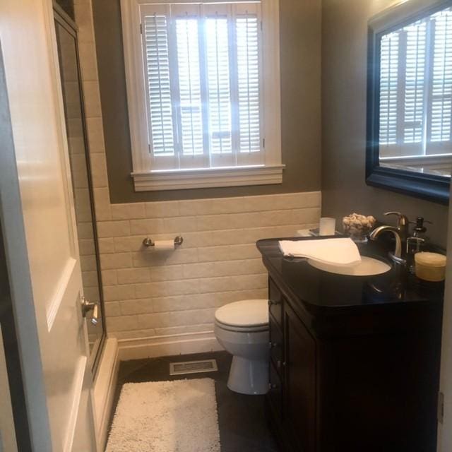 bathroom with vanity, a wainscoted wall, visible vents, toilet, and a shower with door