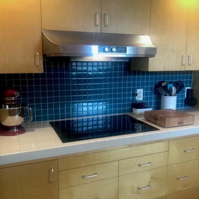 kitchen featuring tile countertops, decorative backsplash, extractor fan, and black electric cooktop