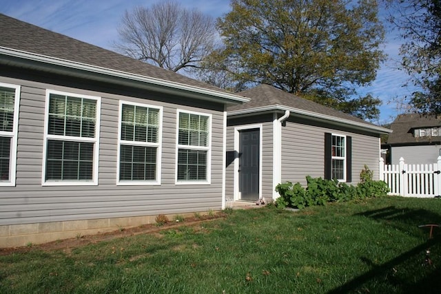 doorway to property featuring a shingled roof, a yard, and fence