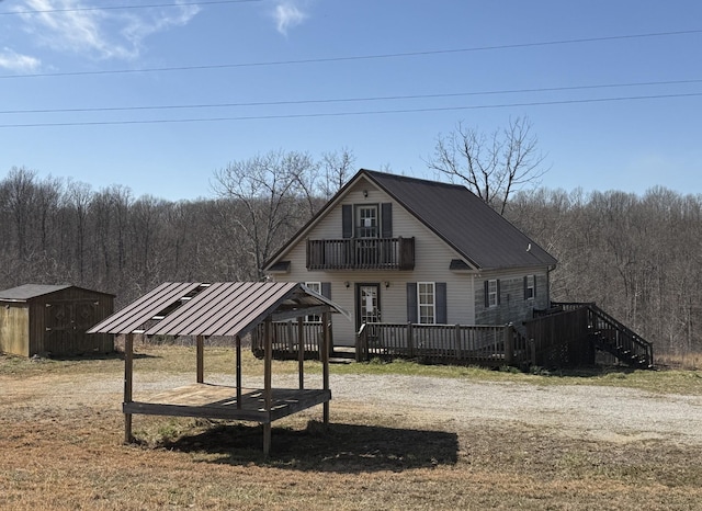 view of front of home featuring metal roof, a view of trees, a balcony, an outdoor structure, and a storage unit