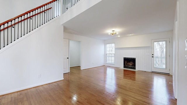 unfurnished living room featuring hardwood / wood-style floors, a tiled fireplace, stairway, and baseboards