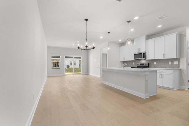 kitchen featuring light wood-style flooring, light countertops, appliances with stainless steel finishes, white cabinetry, and tasteful backsplash