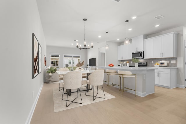 kitchen featuring light wood-style flooring, a kitchen breakfast bar, backsplash, appliances with stainless steel finishes, and light countertops