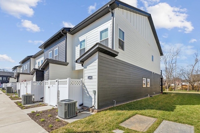 view of property exterior with central air condition unit, board and batten siding, a yard, and fence