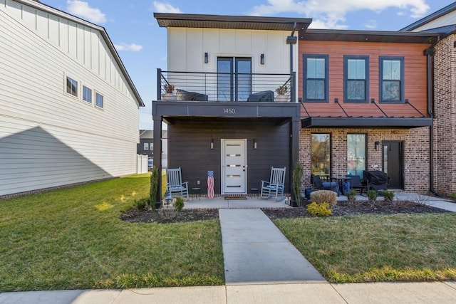 view of front facade featuring brick siding, board and batten siding, a front lawn, and a balcony