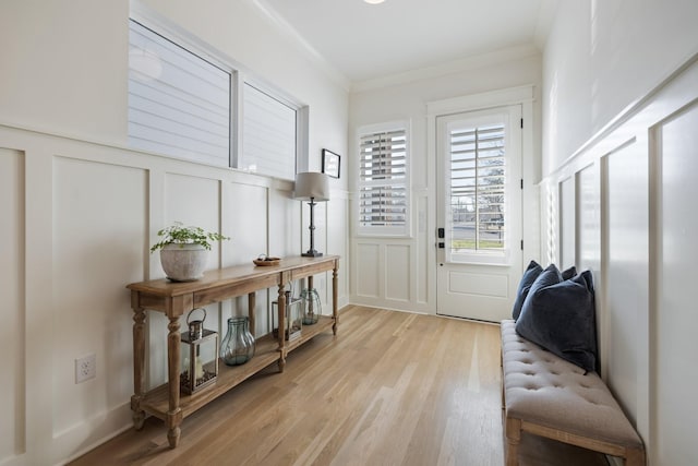 entrance foyer with light wood finished floors, wainscoting, crown molding, and a decorative wall