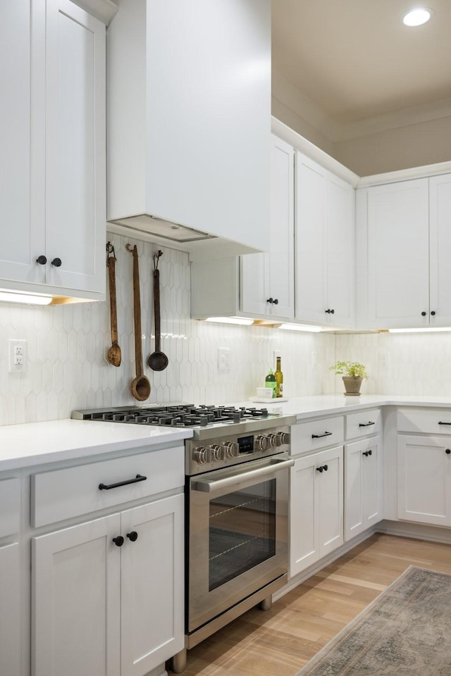 kitchen with stainless steel range with gas stovetop, range hood, light wood-type flooring, and decorative backsplash