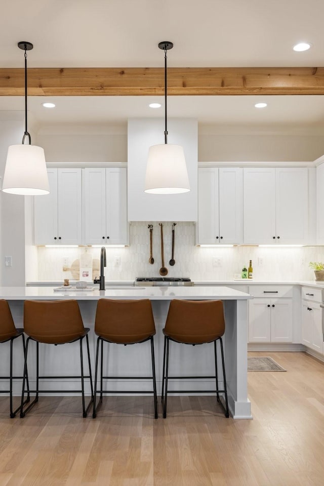 kitchen featuring a breakfast bar, beamed ceiling, light wood-style flooring, and white cabinets