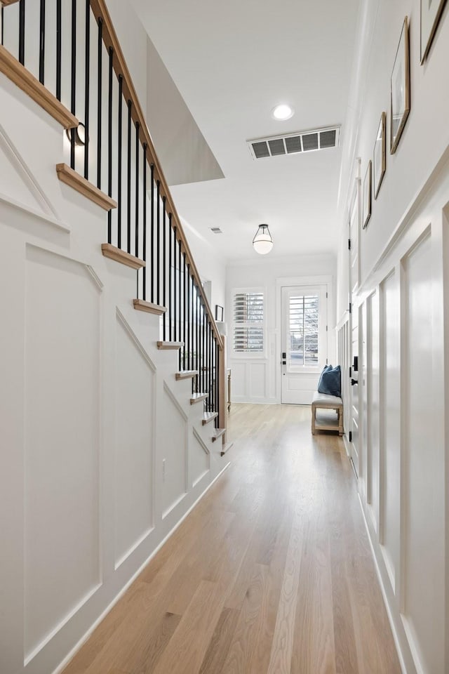 entryway with visible vents, light wood-type flooring, a decorative wall, and stairs