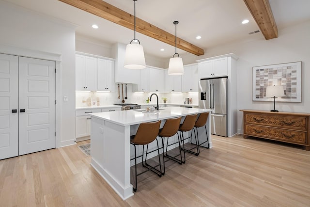 kitchen with a kitchen bar, a center island with sink, a sink, high quality fridge, and light wood finished floors