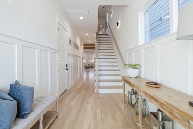 entryway with stairway, a decorative wall, light wood-style flooring, and visible vents