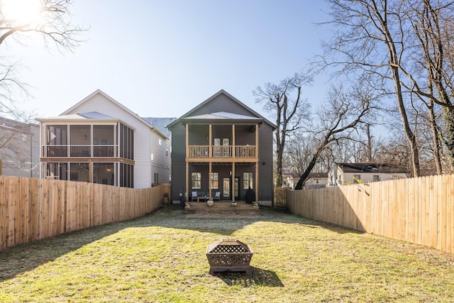 rear view of house featuring a sunroom, a fire pit, a lawn, and a fenced backyard