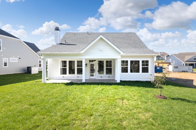 back of property featuring a patio area, a lawn, a chimney, and roof with shingles