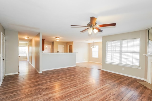 unfurnished living room featuring ceiling fan with notable chandelier, a fireplace with flush hearth, light wood-style floors, and baseboards