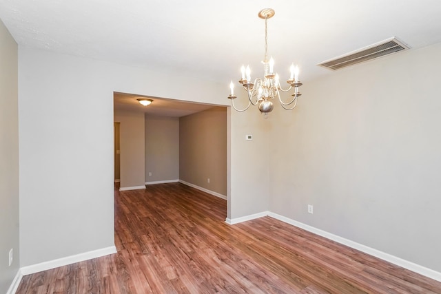 unfurnished room featuring wood finished floors, visible vents, a chandelier, and baseboards