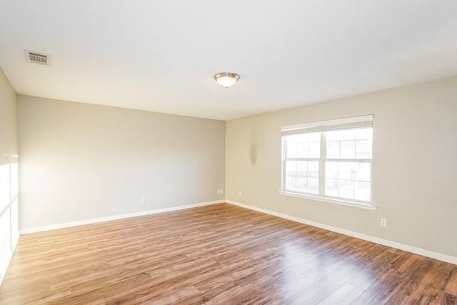 empty room with light wood finished floors, visible vents, and baseboards